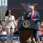 Nicki Minaj standing on stage with Donald Trump, smiling and gesturing to the audience, at a political event showing her support for the former president.